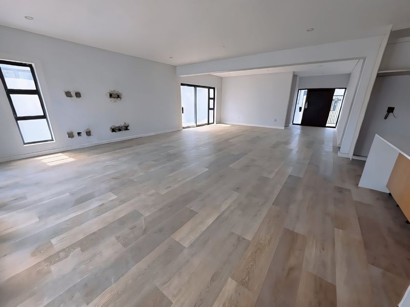 Spacious open-plan living area featuring light-toned engineered timber flooring, recessed lighting, and modern aluminium sliding doors, currently awaiting final wall finishing and electrical trim.
