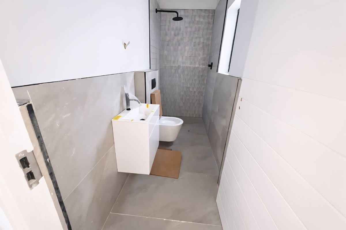 A modern, newly installed bathroom featuring a wall-mounted vanity, basin, and toilet with contemporary grey tiling and black fixtures, currently in the final stages of completion.