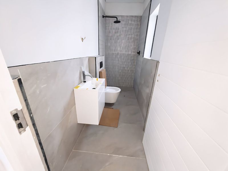 A modern, newly installed bathroom featuring a wall-mounted vanity, basin, and toilet with contemporary grey tiling and black fixtures, currently in the final stages of completion.