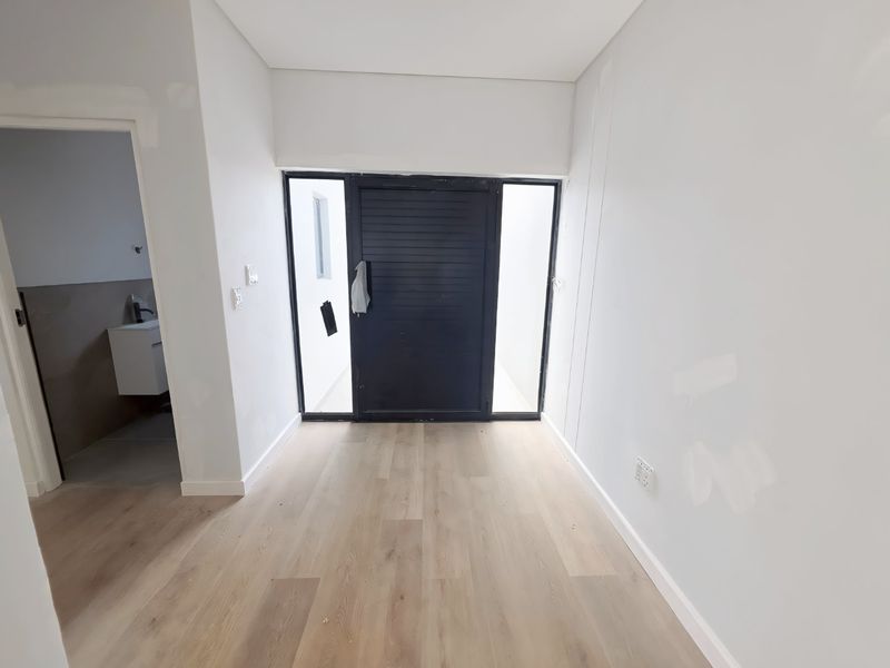 A bright, empty entrance hall featuring modern laminate flooring and a contemporary black-framed front door with side lights, currently awaiting final wall finishing.
