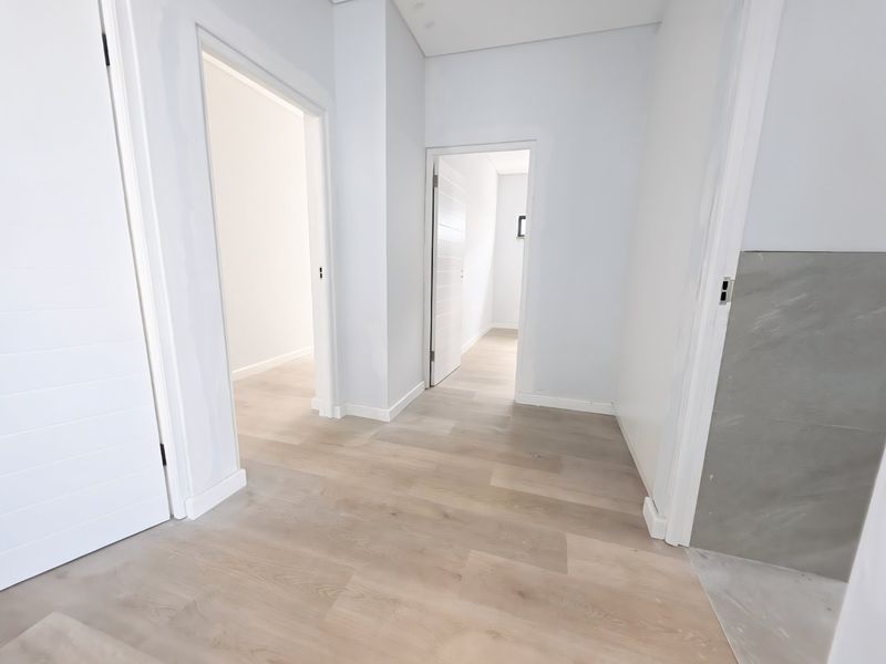 A bright, modern hallway featuring light-toned laminate flooring, clean white walls, and multiple internal doorways leading to adjacent rooms.