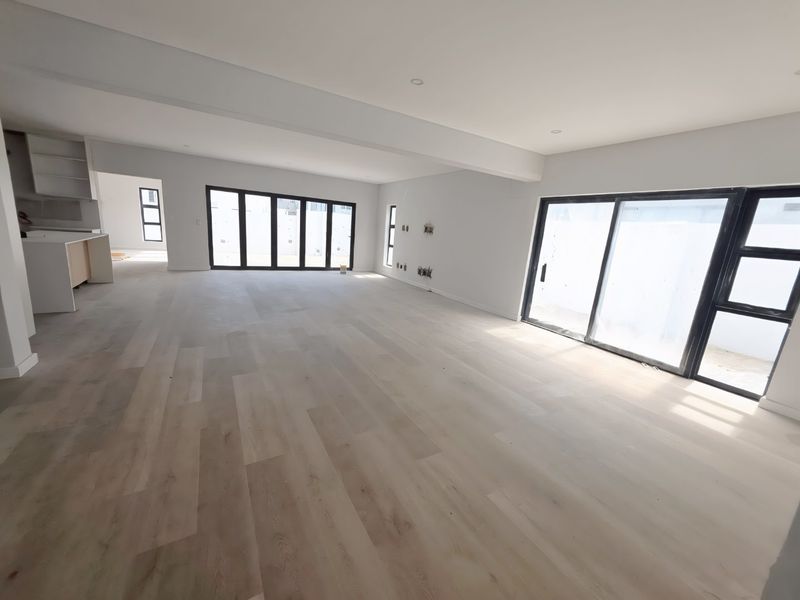 Spacious open-plan living area featuring modern laminate flooring, recessed lighting, and large sliding glass doors providing ample natural light and outdoor access.