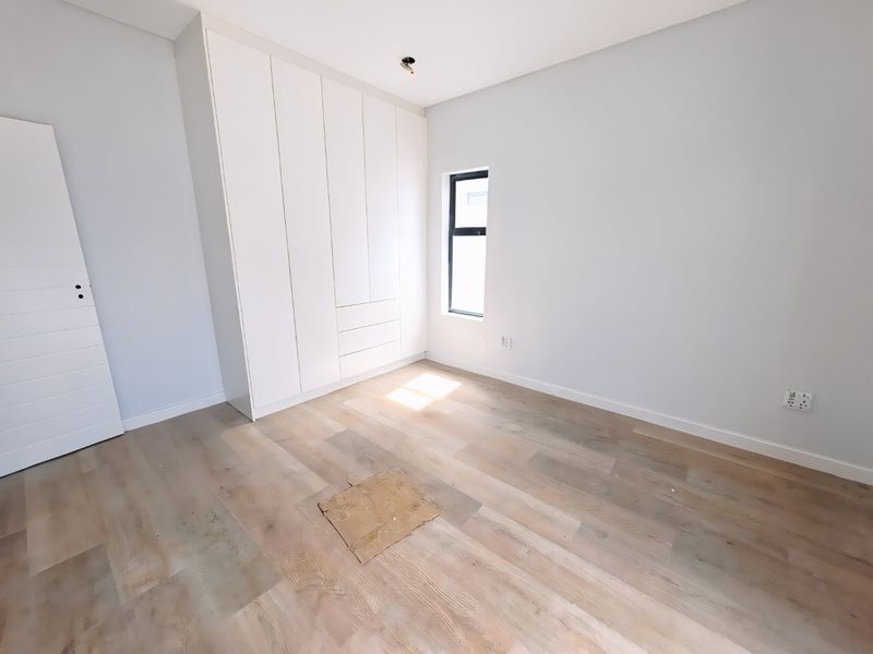 A bright, empty bedroom featuring modern built-in cupboards, light-toned laminate flooring, and a clean, minimalist aesthetic ready for personalization.