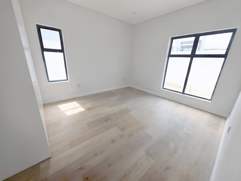 A bright, empty bedroom featuring light-toned engineered timber flooring, modern aluminium-framed windows, and clean white walls, ready for personalization.