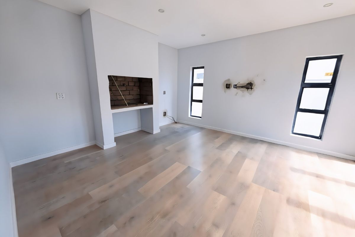 An empty living room featuring light-toned laminate flooring, a built-in fireplace, and recessed lighting, currently requiring minor wall repairs.