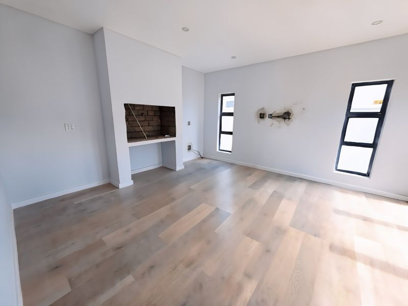 An empty living room featuring light-toned laminate flooring, a built-in fireplace, and recessed lighting, currently requiring minor wall repairs.
