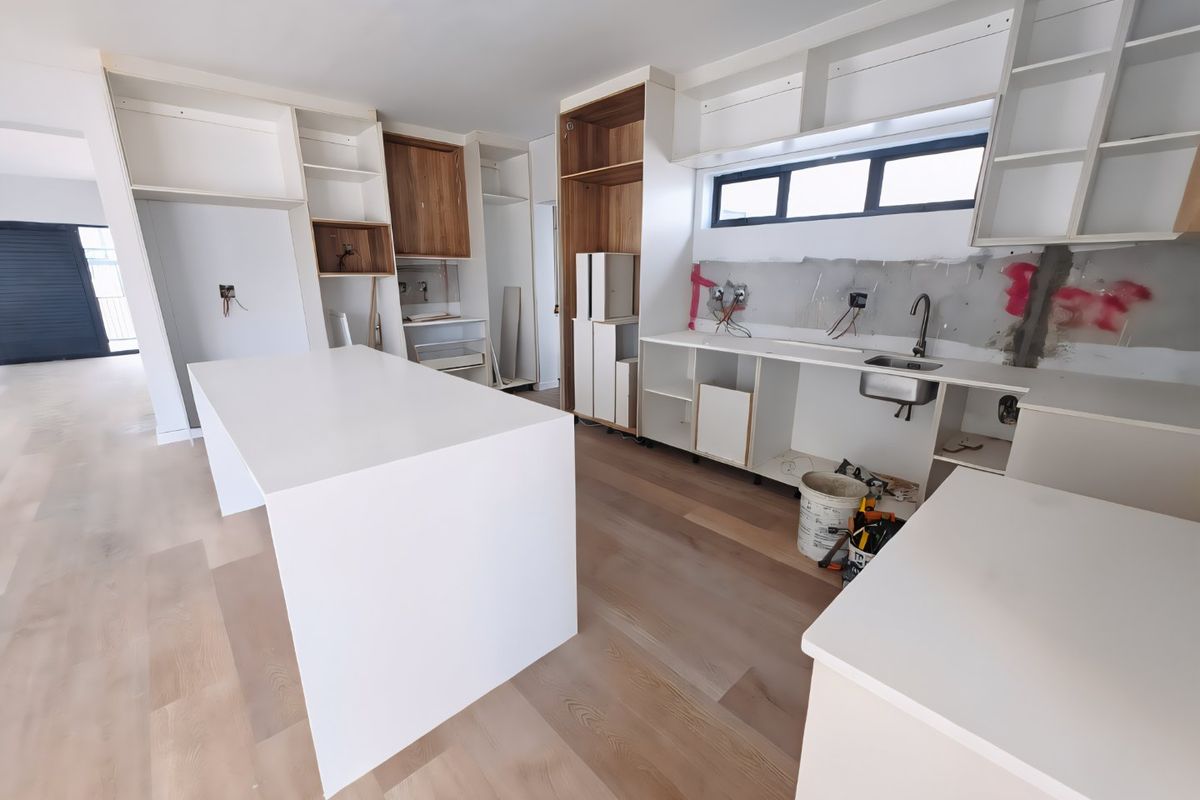 An unfinished kitchen space featuring a central island, built-in cabinetry, and an installed sink, currently undergoing renovation with exposed walls and wiring.