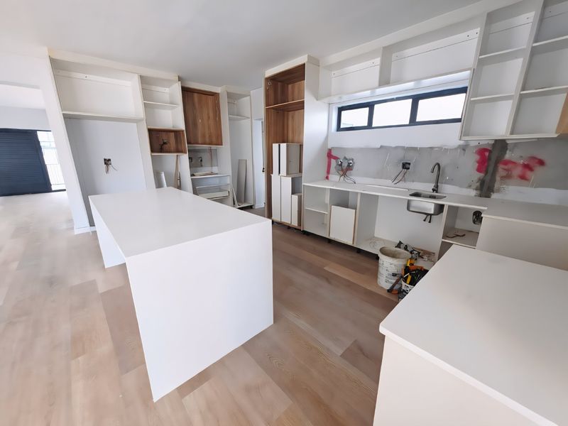 An unfinished kitchen space featuring a central island, built-in cabinetry, and an installed sink, currently undergoing renovation with exposed walls and wiring.