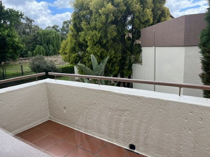 A private balcony featuring tiled flooring and a metal balustrade, offering an elevated view of the surrounding greenery and trees.