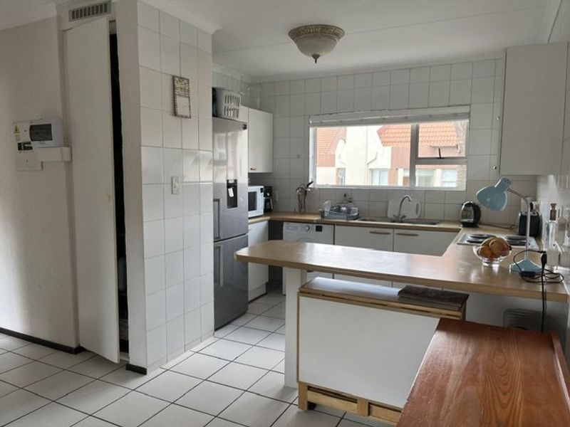 A functional kitchen featuring tiled flooring, ample built-in cabinetry, a breakfast bar, and a tiled splashback, offering a practical layout for daily use.
