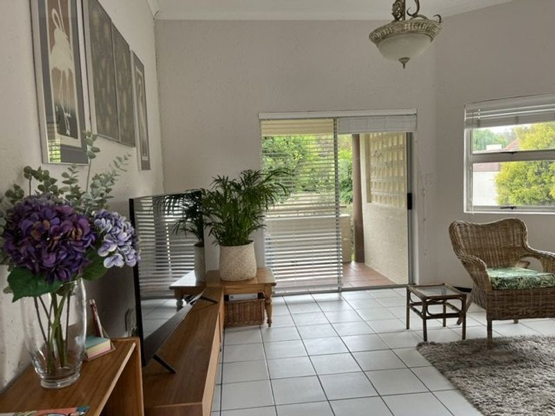 A living room featuring tiled flooring, a sliding glass door leading to a patio, and natural light from a side window.