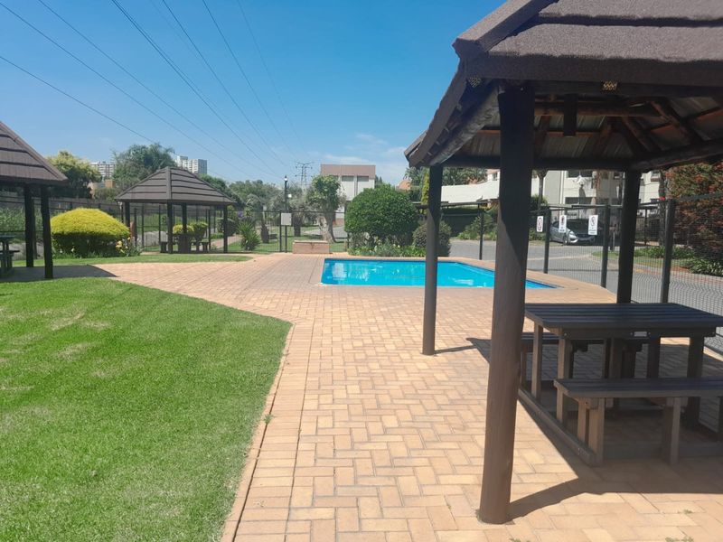 Communal pool area featuring a swimming pool, paved patio space, and multiple thatched gazebos set within a well-maintained garden environment.