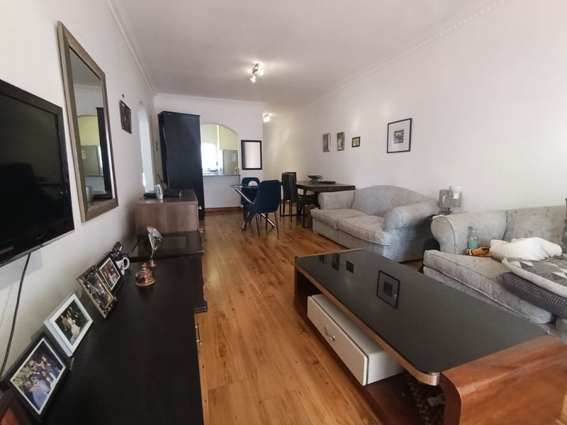 An open-plan living and dining area featuring laminate flooring, coved ceilings, and a connecting archway leading to the kitchen space.