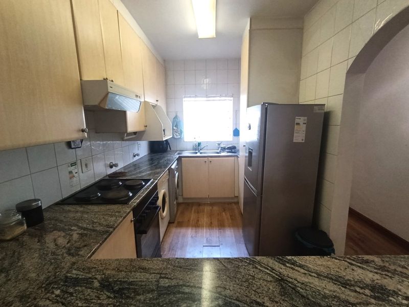 A functional kitchen featuring granite countertops, light wood cabinetry, a built-in electric hob, and an integrated sink area with tiled splashbacks.
