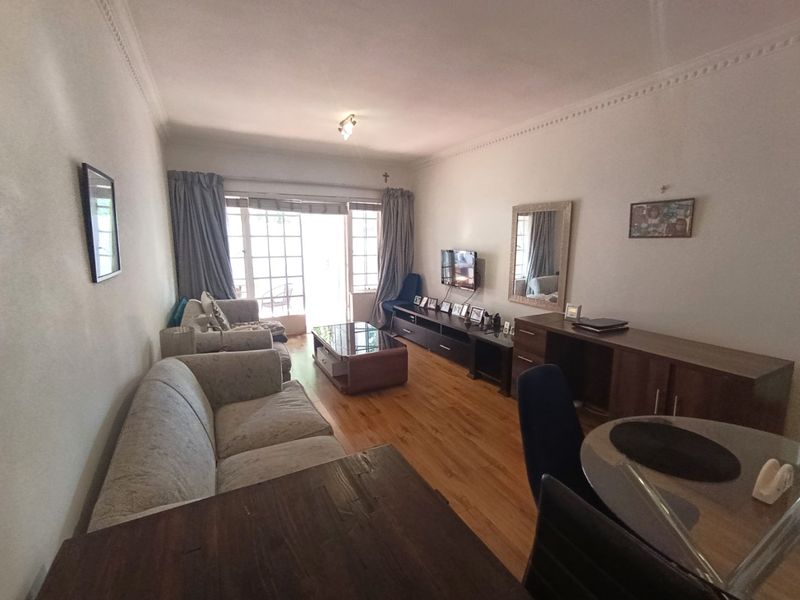 A living room featuring laminate flooring and crown molding, with a sliding glass door providing access to an outdoor area.