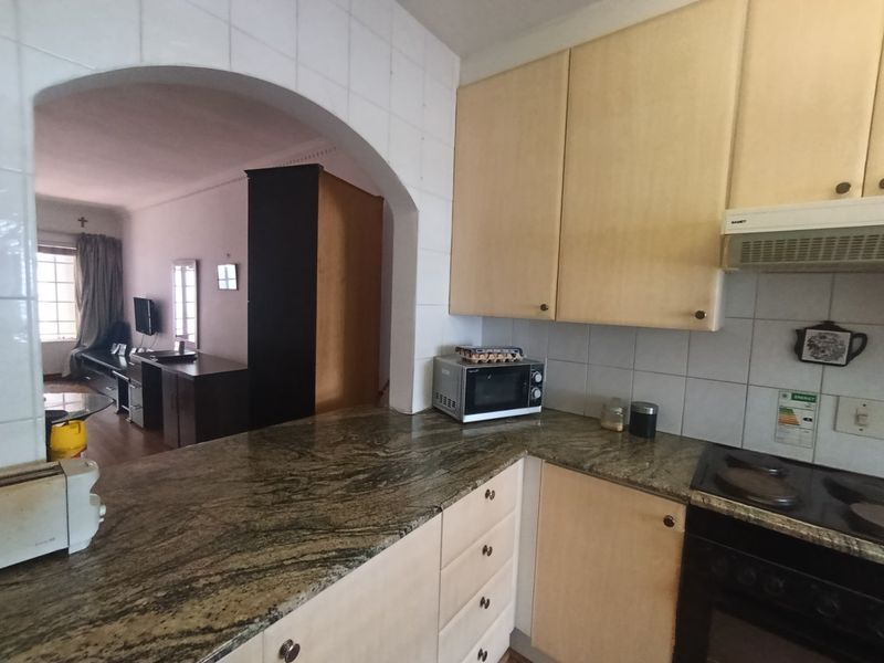 Open-plan kitchen featuring granite countertops, built-in cabinetry, and an electric hob, seamlessly connected to the living area through a classic arched doorway.