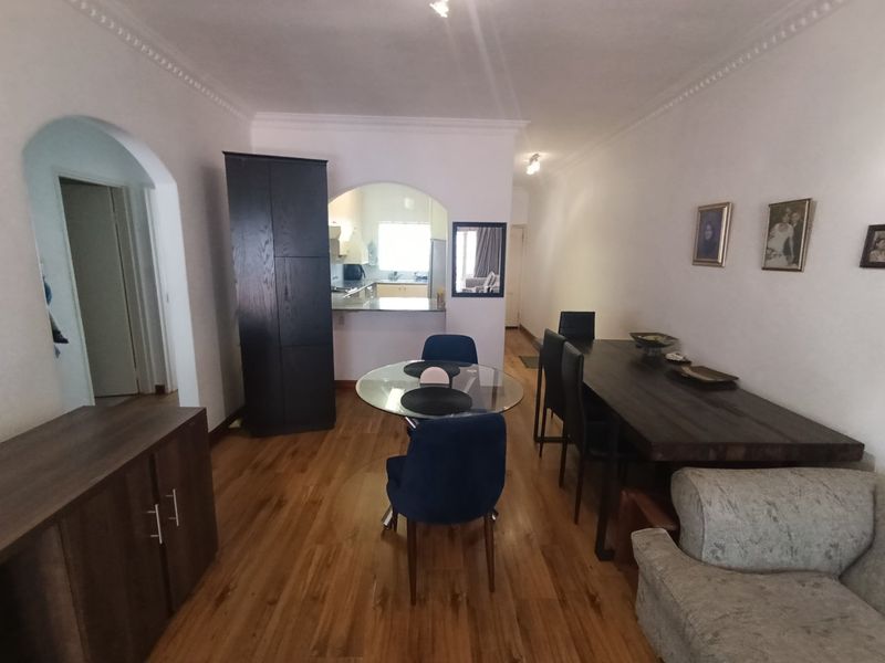 Open-plan living and dining area featuring laminate flooring, coved ceilings, and an arched entryway leading to a functional kitchen space.