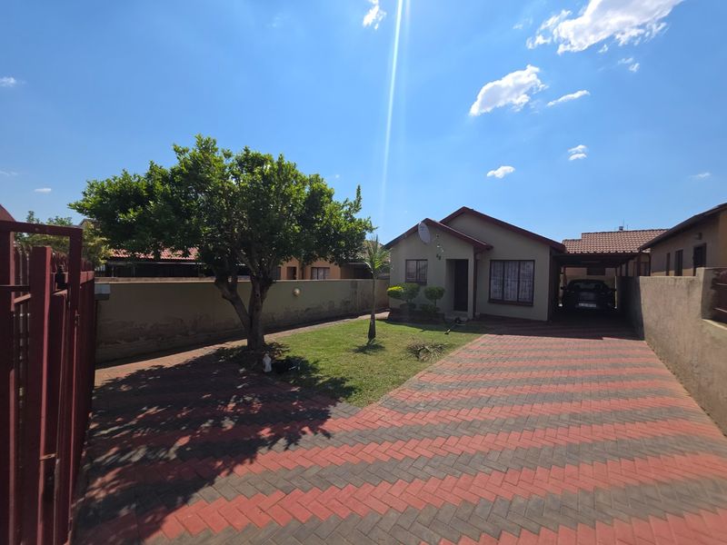 Front view of a residential property featuring a paved driveway, a carport, and a landscaped front garden with a boundary wall.