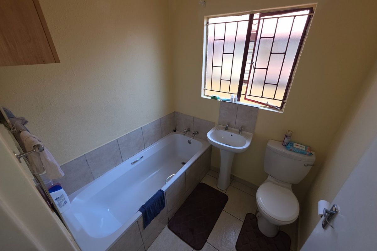 A functional bathroom featuring a bathtub, pedestal basin, and toilet with tiled splashbacks and security bars on the window.
