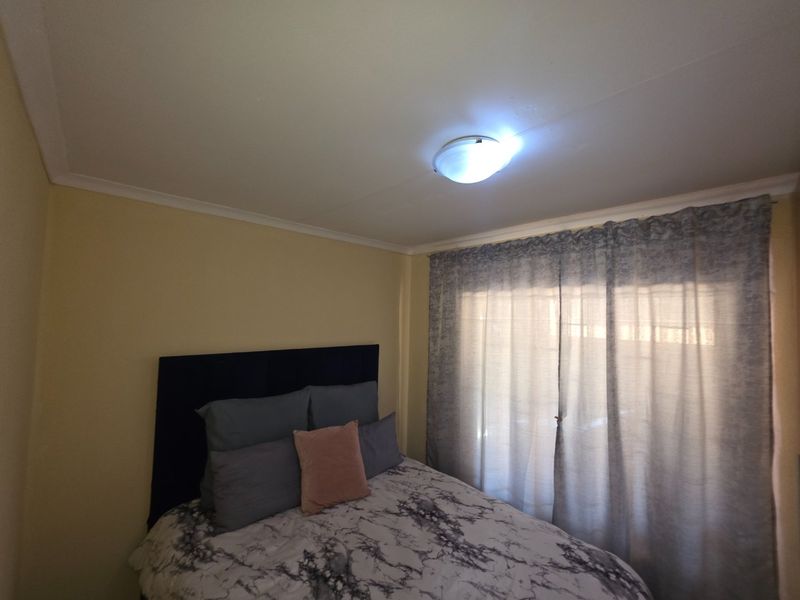 A standard bedroom featuring neutral wall finishes, ceiling cornicing, and a central flush mount light fixture with natural light filtering through window curtains.