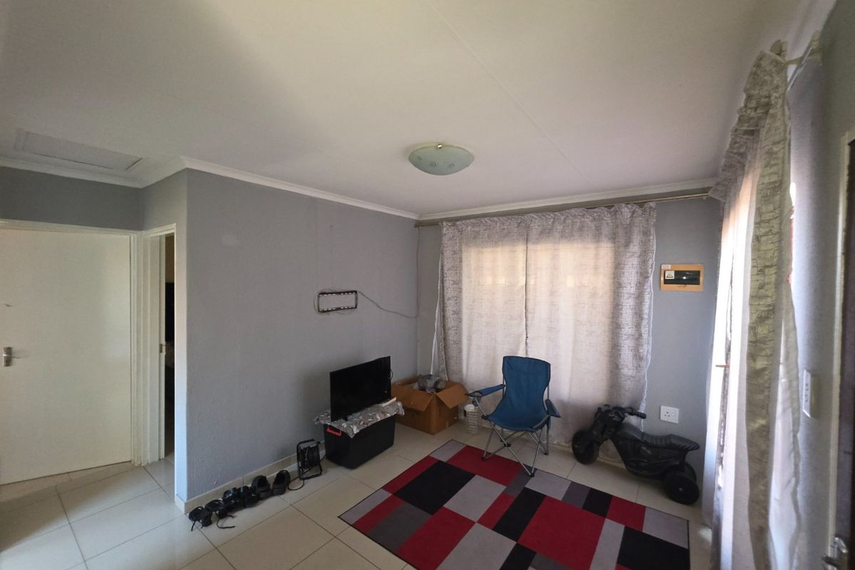 A living room featuring neutral grey walls, tiled flooring, and natural light through window curtains, providing a functional and versatile living space.