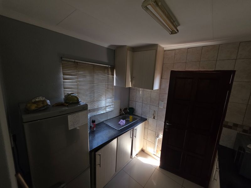 A compact scullery area featuring built-in cabinetry, a stainless steel sink, tiled splashbacks, and tiled flooring, providing functional utility space.