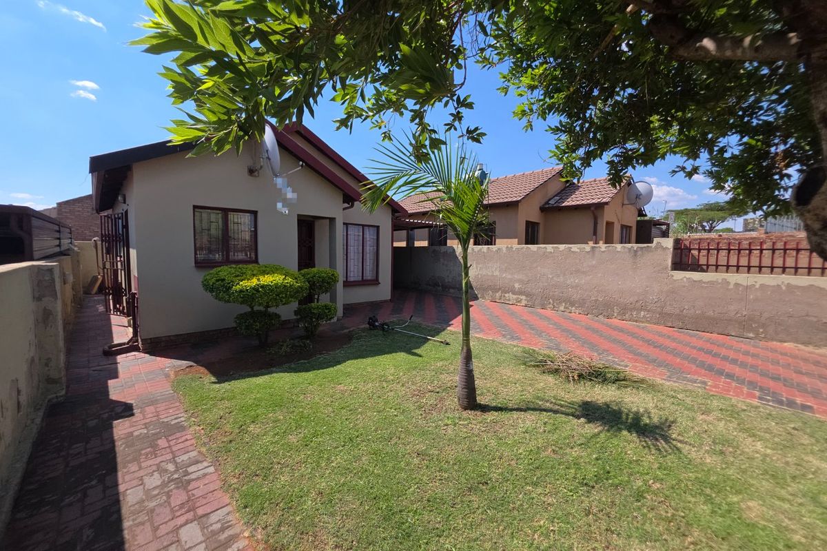 Rear exterior view of the property featuring a paved driveway, small lawn area, and boundary wall with security features.
