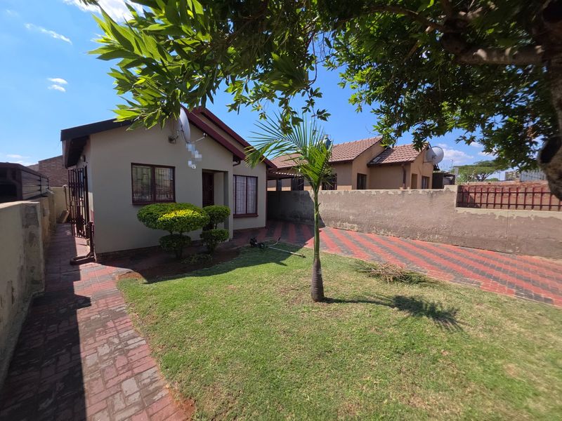 Rear exterior view of the property featuring a paved driveway, small lawn area, and boundary wall with security features.