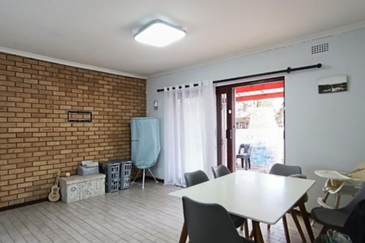 A living area featuring an exposed brick wall, tiled flooring, and a sliding glass door providing access to the outdoor patio.