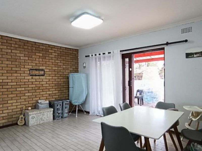 A living area featuring an exposed brick wall, tiled flooring, and a sliding glass door providing access to the outdoor patio.