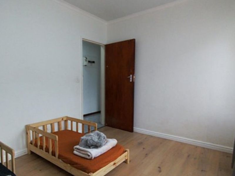 A simple bedroom featuring light-toned laminate flooring, white walls, and a classic timber door, offering a clean and neutral space.