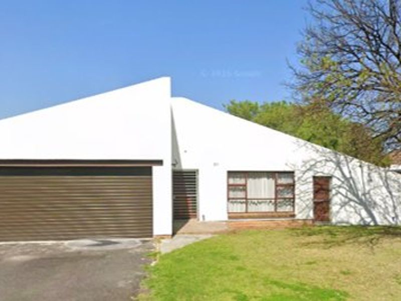 Front elevation of a single-story house featuring a roller garage door, asphalt driveway, and white rendered facade.