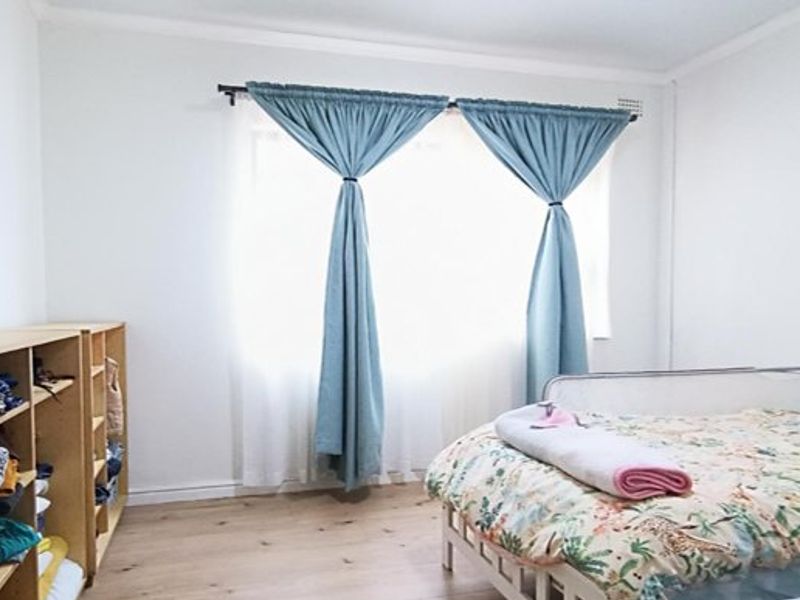A bright bedroom featuring light-toned laminate flooring and a large window with fitted curtain rods.