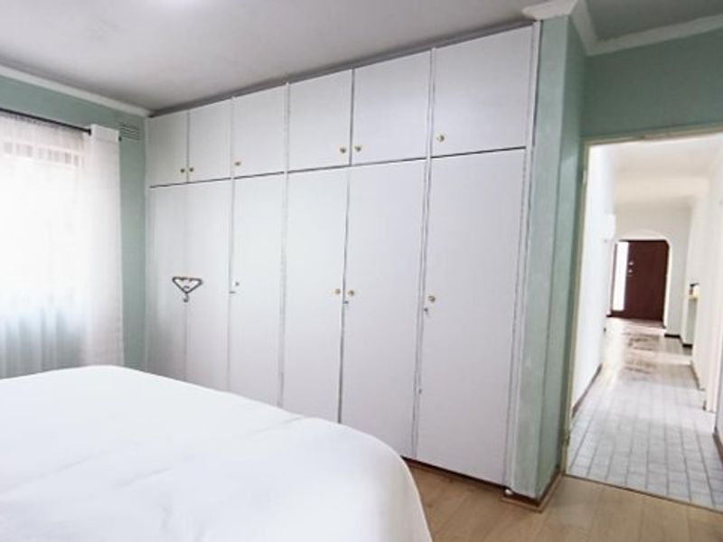 A bedroom featuring extensive floor-to-ceiling built-in cupboards, laminate flooring, and neutral wall finishes, with a view into the adjacent hallway.
