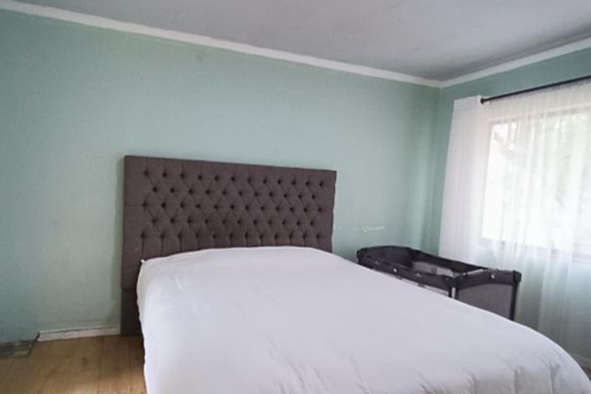 A bedroom featuring laminate flooring and light green walls, offering a functional space with natural light from the window.