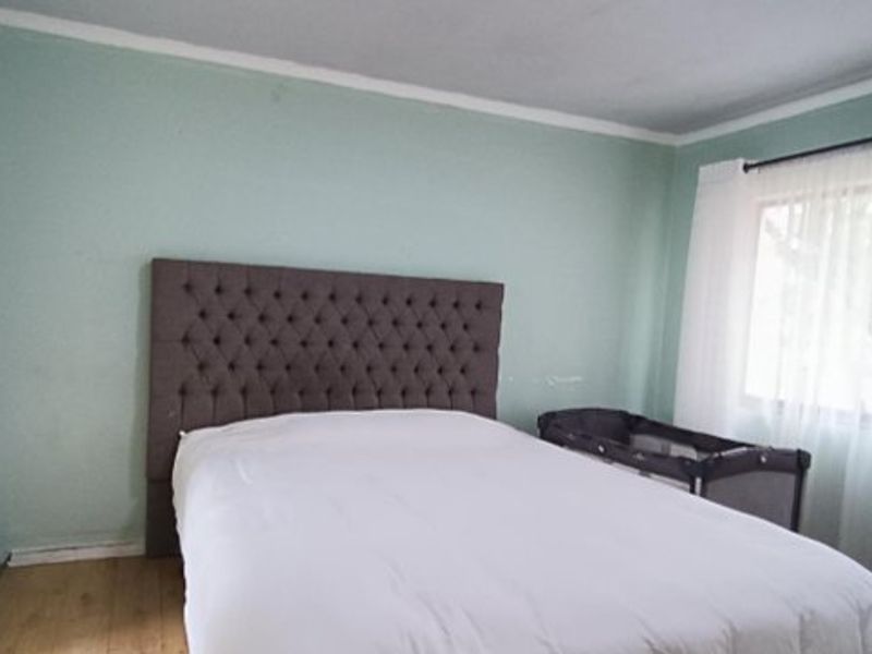 A bedroom featuring laminate flooring and light green walls, offering a functional space with natural light from the window.