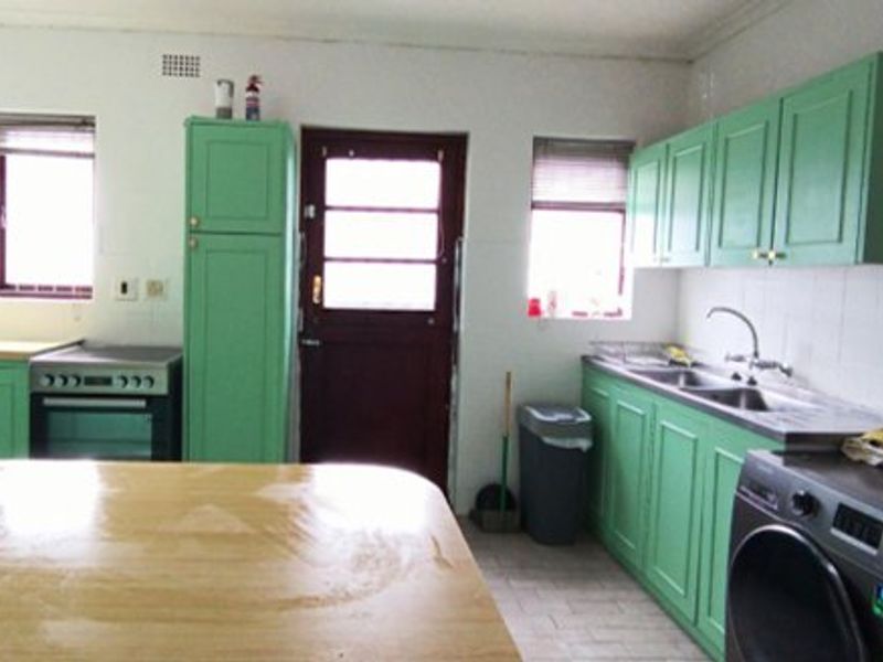 A functional kitchen featuring green cabinetry, a double sink, tiled backsplash, and a freestanding oven with direct access to the exterior.