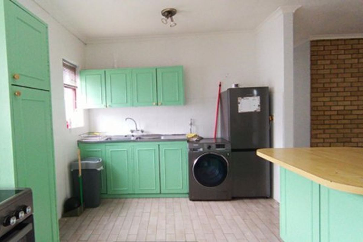 A functional kitchen featuring mint green cabinetry, a breakfast bar, tiled flooring, and an exposed brick feature wall, offering potential for modern renovation.