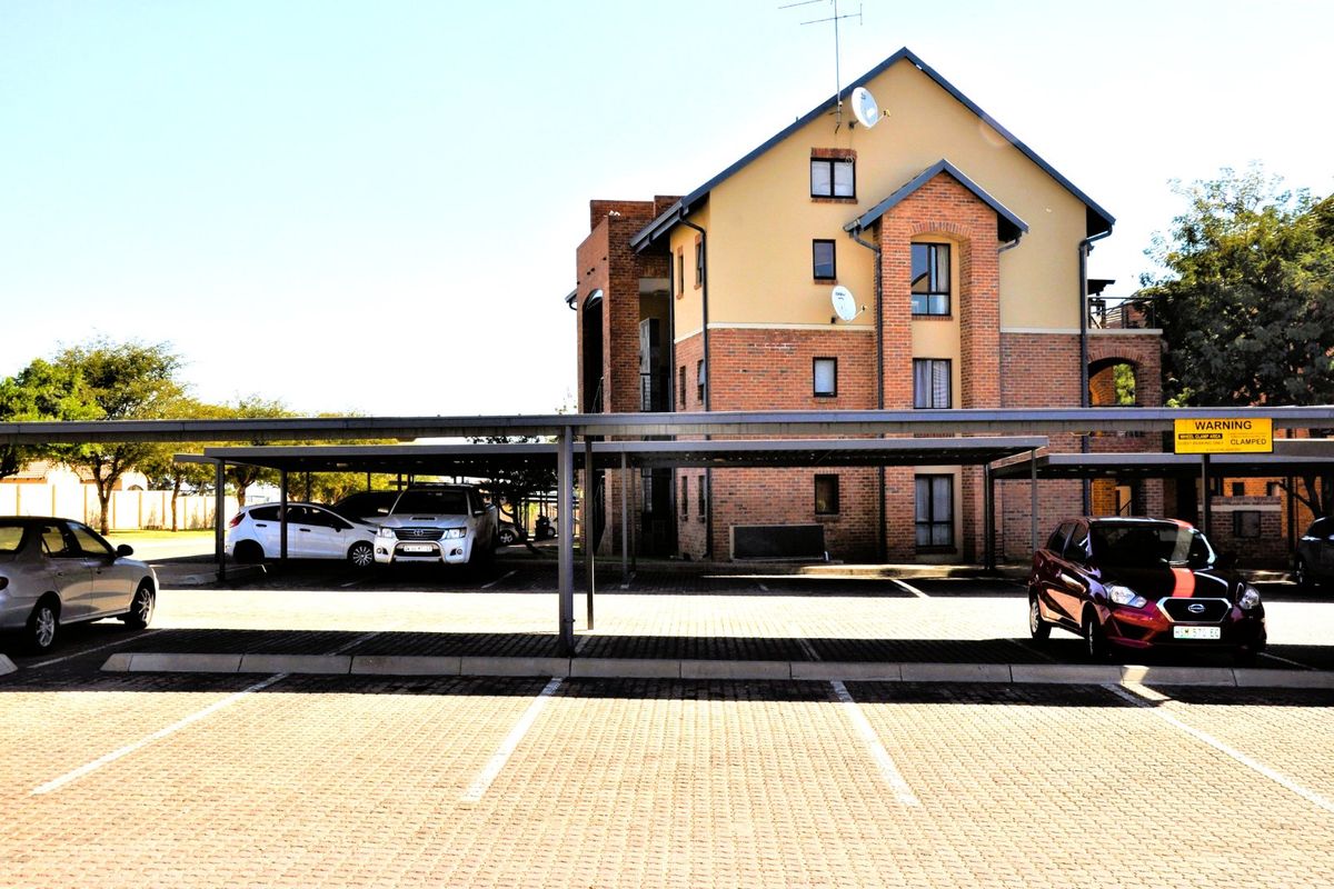 A multi-story residential building featuring a brick and plaster facade with dedicated covered parking bays in the foreground.