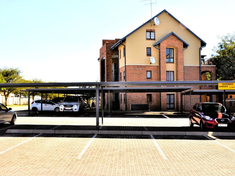 A multi-story residential building featuring a brick and plaster facade with dedicated covered parking bays in the foreground.