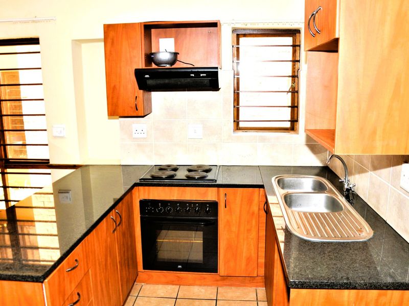 A functional kitchen featuring wooden cabinetry, granite countertops, a built-in oven with hob, and a double stainless steel sink with tiled splashbacks.