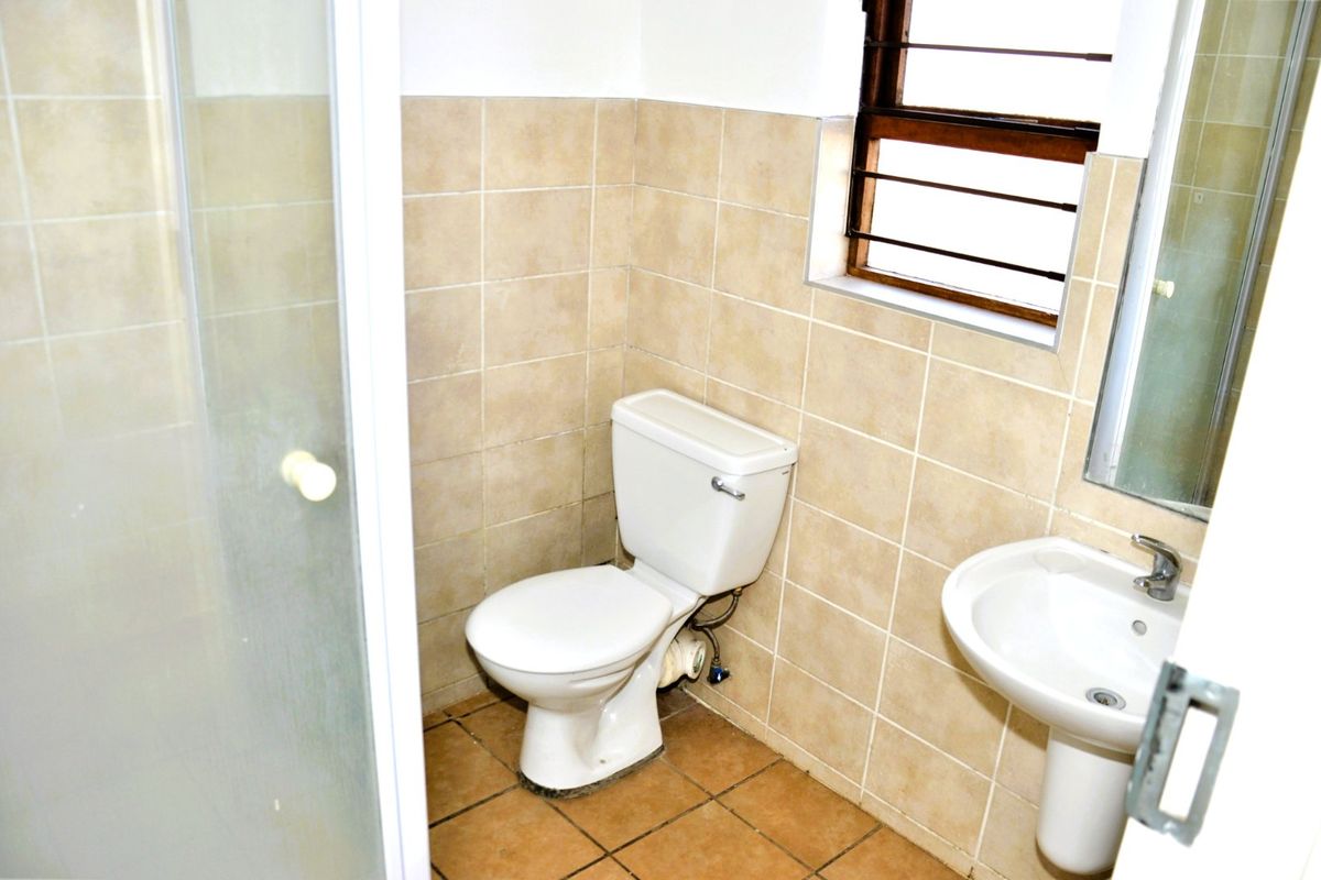 A functional bathroom featuring a shower enclosure, pedestal basin, and toilet with neutral ceramic wall and floor tiling.