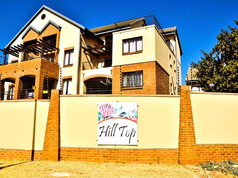 Front view of the Hill Top residential complex featuring multi-story brick architecture, private balconies, and secure perimeter wall with electric fencing.