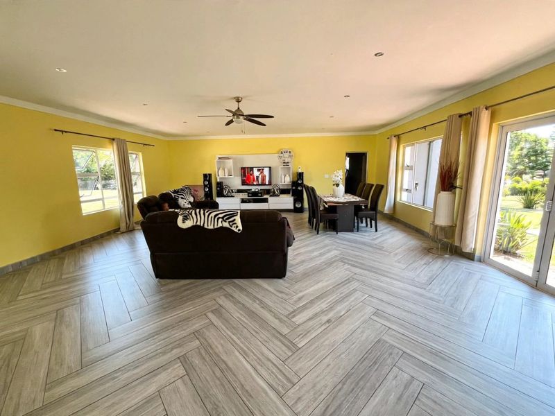 Spacious open-plan living and dining area featuring modern herringbone-patterned floor tiles, recessed lighting, and large windows providing ample natural light.