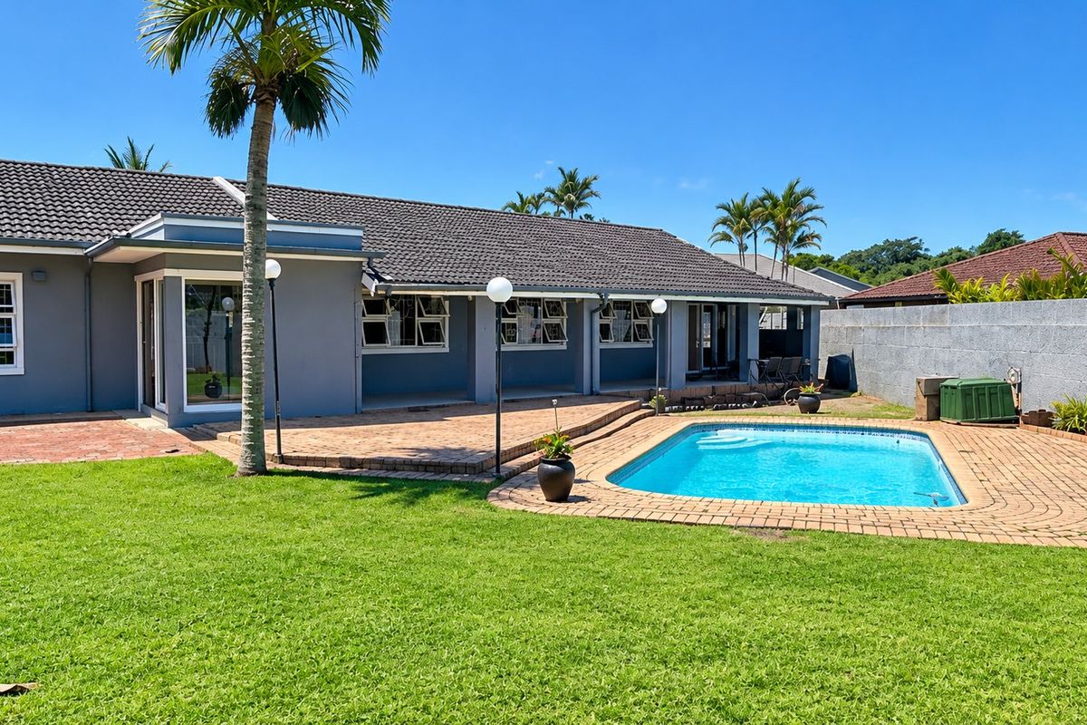 Rear view of the property featuring a well-maintained swimming pool, brick paved patio area, and a spacious garden with boundary walling.