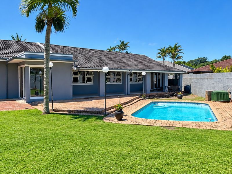 Rear view of the property featuring a well-maintained swimming pool, brick paved patio area, and a spacious garden with boundary walling.