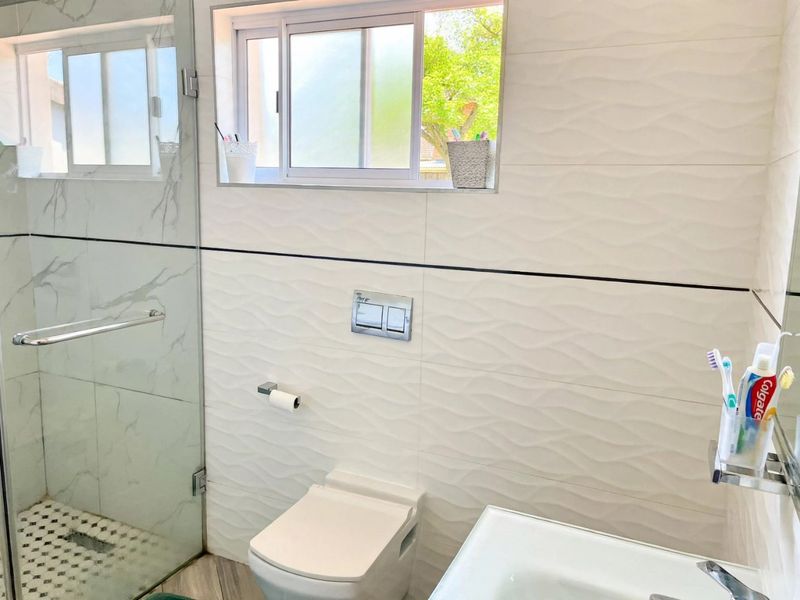 Modern bathroom featuring a walk-in shower with glass screen, wall-hung toilet with concealed cistern, and contemporary textured wall tiling.