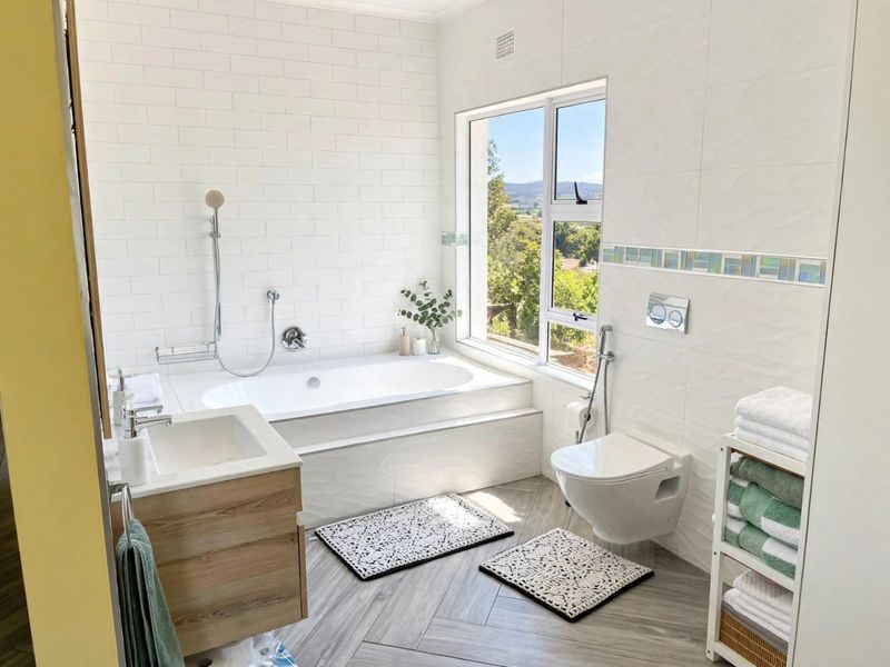 Modern bathroom featuring a built-in bathtub, wall-mounted toilet, vanity cabinet, and large window with scenic views, finished with contemporary tiling.