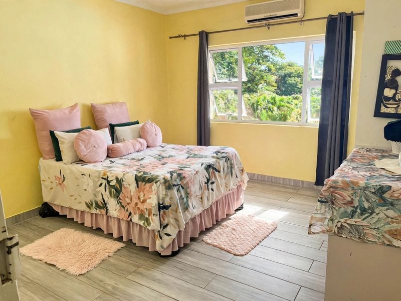 A bright bedroom featuring tiled flooring, an installed air conditioning unit, and large windows providing natural light and garden views.