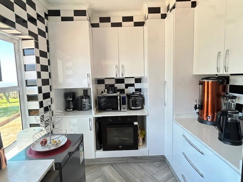 A compact kitchen featuring high-gloss white cabinetry, stone countertops, and a distinctive black and white checkered tile backsplash with modern floor tiling.